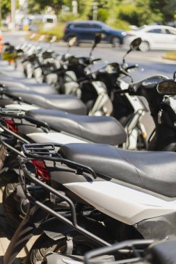 Park halindeki birkaç scooter, hareketli bir cadde kavşağında, temiz mavi gökyüzünün altında canlı bir şehir atmosferini yakalıyor..