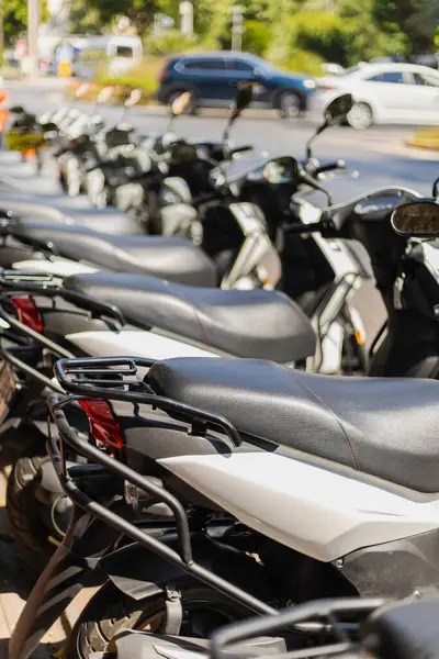 Park halindeki birkaç scooter, hareketli bir cadde kavşağında, temiz mavi gökyüzünün altında canlı bir şehir atmosferini yakalıyor..