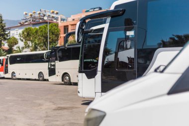 Açık mavi gökyüzünün altında sayısız otobüs bir ulaşım merkezine park edilmiştir. Araçların boyut ve renkleri farklı. Organize bir park alanı faaliyet gösteriyor..