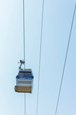 Bir gökyüzü gondolu yerden yüksek kablolar boyunca sorunsuzca süzülür. Parlak mavi gökyüzü sakin atmosferi yükselterek çarpıcı manzaralar üzerinde huzurlu bir yolculuk sunuyor..