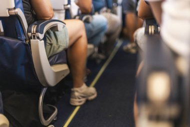 Yolcular uçaktaki koltuklarında dinlenerek, bacaklarına ve koridora odaklanırlar. Atmosfer sakin, parlak bir yaz gününde rahat bir uçuş deneyimi olduğunu gösteriyor..