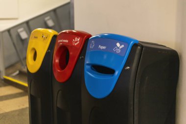 Kağıt, genel atık ve plastik olarak etiketlenmiş renkli geri dönüşüm kutuları kamu alanındaki bir duvara dayanarak geri dönüşüm ve atık ayrımını teşvik etmektedir..