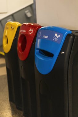 Kağıt, plastik ve genel atık için etiketlenmiş üç geri dönüşüm kutusu halka açık bir koridorda düzenleniyor. Her bir çöp kutusu renk kodlu: kırmızı, sarı ve mavi, uygun atımı destekliyor.