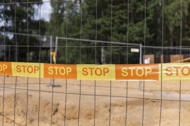 İnşaat alanı parlak turuncu uyarı bandıyla işaretlenir. Durur, güneşli bir günde ormanlık alanda kazı alanı etrafında bir bariyer oluşturur..