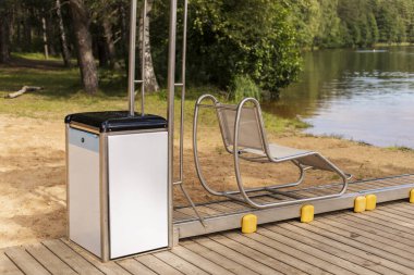 Özel olarak tasarlanmış bir sürgülü sandalye ahşap bir rıhtımın yanında duruyor ve engellilerin suya girmesi için kolay bir erişim sağlıyor. Huzurlu göl manzarası deneyimi güçlendirir..