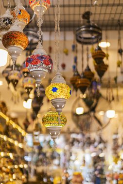 Canlı bir pazarda tavandan sarkan parlak renkli fenerler, alışverişçiler akşamları çeşitli tezgahları keşfederken canlı bir atmosfer yaratıyor..