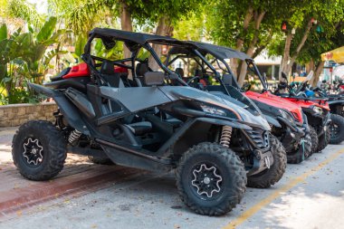 Birkaç off-road aracı güneşli hava altında bir yürüyüş yolu boyunca düzgün bir şekilde park edilmiştir. Yeşillikler bölgeyi çevreleyerek ziyaretçiler için canlı bir atmosfer oluşturuyor..