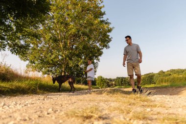 Bir adam ve küçük oğlu kahverengi köpekleri ile huzurlu bir toprak yolda yürüyorlar. Sıcak güneş ışığından ve çevrelerindeki doğanın güzelliğinden zevk alırlar. Sevimli anılar yaratırlar..