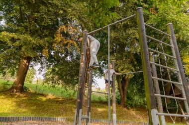 Bir baba oğlunun ağaçlarla çevrili parka tırmanmasına yardım eder. Dışarıda keyifli anları paylaşıyorlar, oyun ve keşif yoluyla bağlarını güçlendiriyorlar..