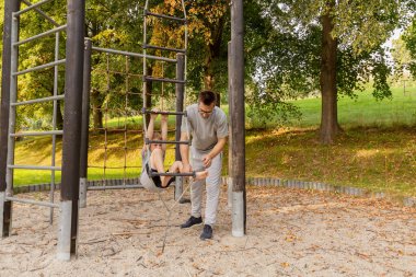 Bir baba ve küçük oğlu oyun alanında birlikte oynuyorlar, yeşillik dolu huzurlu doğal ortamda bağ kurma anlarını teşvik ediyorlar. Aktif eğlenceye dalmışlar..