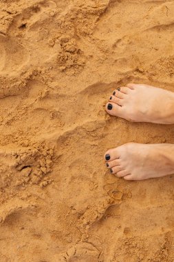 Çıplak ayaklar güneşli bir sahil gününde yumuşak, sıcak kuma batar. Altın tanecikler, deniz kenarındaki atmosferin tadını çıkarırken rahat ve rahat bir ortam sunuyor..