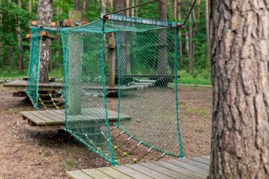 Ahşap ve ağdan yapılmış sağlam bir tırmanma iskeleti yemyeşil bir orman bölgesinde oturur ve çocukları açık hava aktivitelerini keşfetmeye ve eğlenmeye davet eder. Çevreleyen ağaçlar huzurlu bir atmosfer sağlıyor..