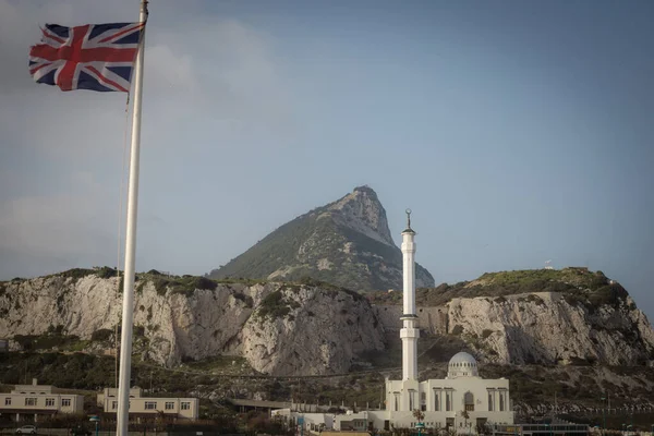 Bir kayanın arkasında İngiliz bayrağı ve camii, Cebelitarık.