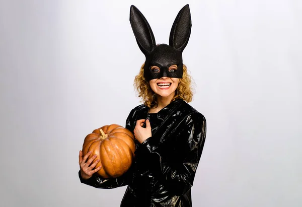 Smiling girl in halloween bunny costume with pumpkin. Sexy woman in rabbit mask with jack-o-lantern