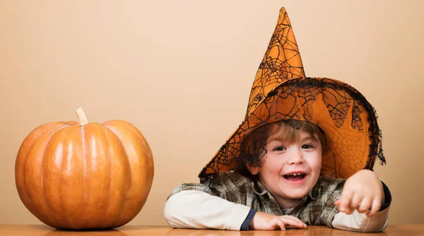 Child in witch hat with halloween pumpkin. Smiling little boy preparation for Halloween holiday