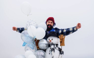 Happy holiday. Bearded man in winter wear with snowman in hat, scarf and mittens with air balloons