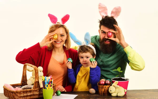 Happy family preparing for Easter. Mother, father and son painting eggs for holidays. Rabbits family on Easter. Happy family in bunny ears painting Easter eggs together. Easter family traditions