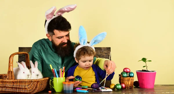 Father and son painting Easter eggs. Cute little child boy wearing bunny ears on Easter day. Happy Easter family painting eggs for holidays. Father and little child boy preparing for Easter holiday
