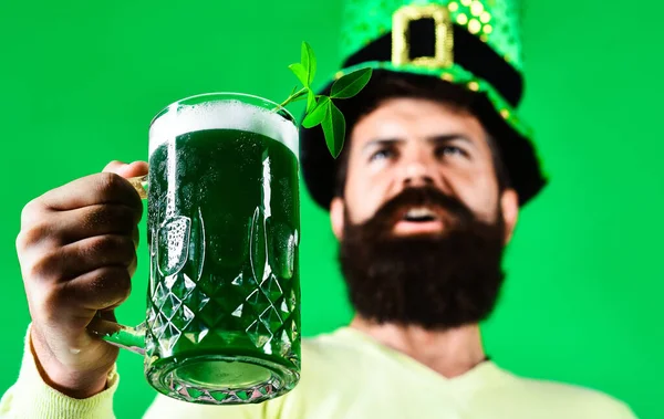 Saint Patricks Day. Green beer with clover. Bearded leprechaun holding mug of green beer pint. Patrick Day pub party celebrating. Ireland tradition. Glass of green beer. Advertising. Selective focus