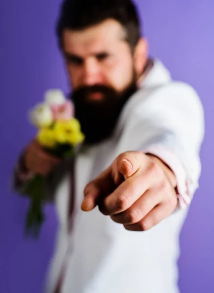 Bearded man with flowers bouquet pointing finger forward. Selective focus on hand. Businessman with flowers showing finger on you. Delivery service. Advertising. Sale. Discount. Birthday celebration