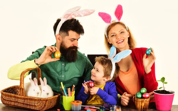 Easter family traditions. Eggs hunt. Mother, father and son preparing for Easter holiday. Happy parents and adorable boy in bunny ears with colorful painted eggs. Family celebrating Easter day
