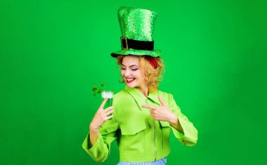 Aziz Patrick Günü. Cüce şapkalı gülümseyen kız yeşil bira bardağını işaret ediyor. Patrick Day 'in bar partisi. Kadın barda bira içiyor. İrlanda geleneği. Yoncalı bir bardak yeşil bira. Reklamcılık