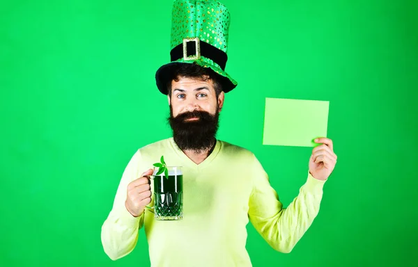 stock image Patricks Day. Bearded man in leprechaun hat with green beer holds advertising board. Saint Patricks Day symbols. Ireland tradition. Patricks Day man in green top hat with mug of beer. Clover in beer