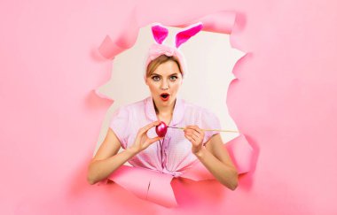 Paskalya kutlaması. Paskalya yumurtası boyayan sürpriz kadın. Av yumurtası. Tavşan kulaklı, pembe yumurtalı ve boya fırçalı bir kız kağıda bakıyor. Paskalya gelenekleri. Paskalya tavşanı. Bahar tatili