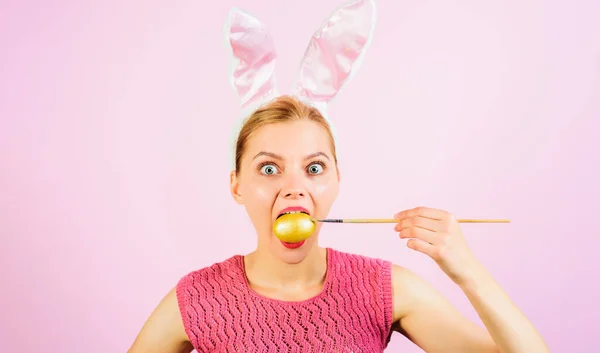 Happy Easter. Funny girl in bunny ears with painted egg in mouth. Sale. Discount. Easter eggs decorating ideas. Surprised woman with yellow egg and paint brush. Easter rabbit girl with colorful egg