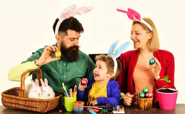 Happy family Easter. Mother, father and son painting eggs for holidays. Rabbits family on Easter. Happy family in bunny ears painting Easter eggs together. Easter family traditions