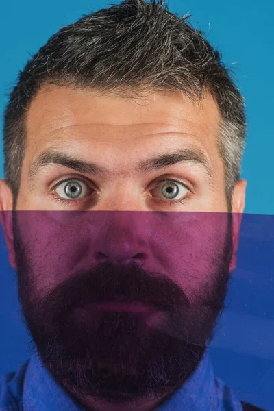 Color concept. Bearded man hiding her face behind colored glass. Serious bearded man partially closed by glass. Vivid colors. Closeup portrait. Fashion man in denim shirt with acolored items