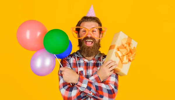 現在の箱や風船と面白い眼鏡や誕生日の帽子で幸せな髭の男 多色の気球とギフトボックスで誕生日を祝うハンサムな男 パーティーの時間だ 祝祭日 — ストック写真