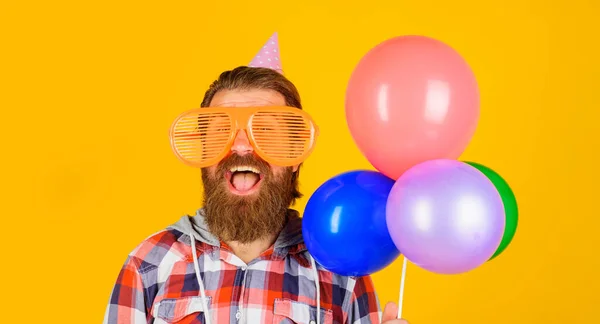パーティー用のメガネと誕生日の帽子の幸せな髭の男 多色の気球で誕生日を祝うハンサムな男 パーティーの時間だ 休日やお祝い 誕生日おめでとう — ストック写真