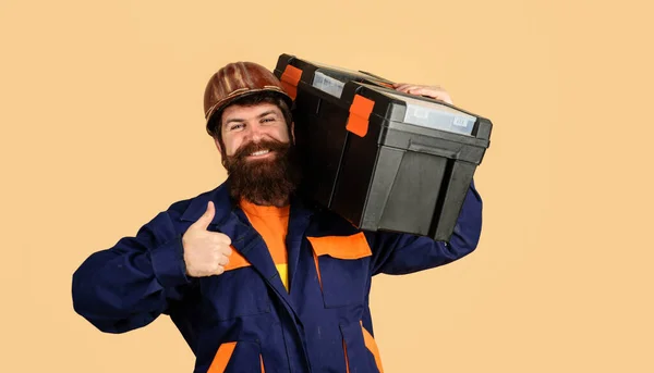 Builder with tool box show thumbs up. Repairman in overalls carry toolbox. Male builder in hardhat with tool box. Builder in protective helmet with toolbox. Tools for repair. Handyman with repair kit