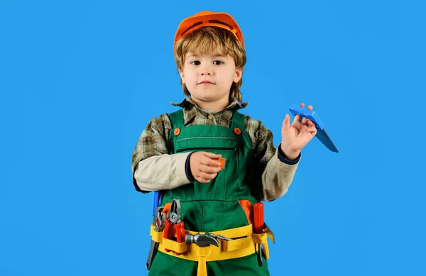Child boy in builder uniform with tool belt. Tools for building. Little kid in overalls and safety helmet with builders tools. Little boy plays construction worker. Little kid repairman with with saw