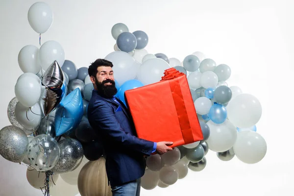 Birthday gift. Happy bearded man with helium balloons and big present box. Birthday party. Business man in suit with big present gift box. Happy businessman with inflatable air balloons and gift box
