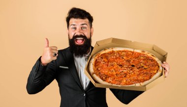Pizzalı sakallı adam baş parmağını gösteriyor. Lezzetli fast food tadı. Lezzetli İtalyan pizzalı bir iş adamı. Takım elbiseli sakallı adam pizzanın tadını çıkarıyor. Pizza teslimatı Yemek, iş yemeği. Sağlıksız beslenme