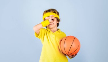 Küçük basketbolcu. Basketbol topuyla gülümseyen çocuk işaret veriyor. Tamam, mükemmel bir sembol. Basketbol topuyla spor giyimli çocuk. Spor malzemeleri. Basketbol antrenmanı. Çocukluk ve spor