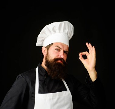 Üniformalı şef ve beyaz önlük işaretini gösteriyor. Tat onaylı yemek pişirme hareketi. Restoran servisini onayladığı için jest yapan sakallı erkek şef. Lezzetli tabelası olan şef.