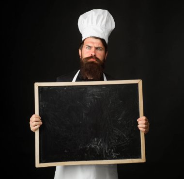 Boş tahtası olan sürpriz bir erkek aşçı. Yemek hazırlama. Sağlıklı menü. Üniformalı aşçı ve boş ilan panosuyla aşçı şapkası. Restorandaki reklam menüsü için boşluk kopyala. Mutfak, yemek, diyet, yemek