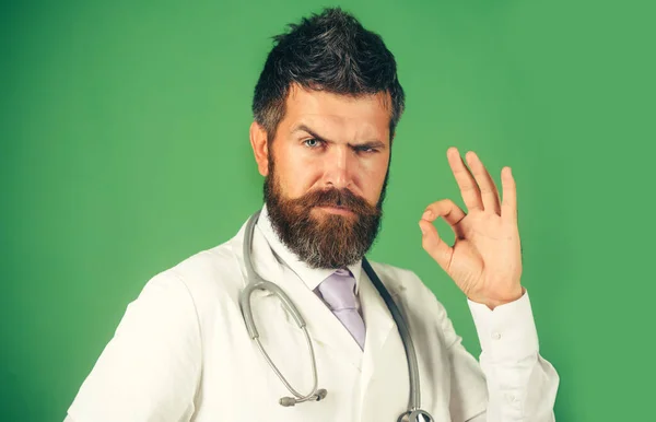 严重的医生显示好迹象 带着听诊器的留胡子男子 身穿白色的医疗外套 带有经认可的标志 医疗保健 身穿军服的男医生 姿势不错 — 图库照片