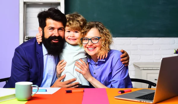 Elementary student. Happy male and female teachers hugging with little schoolboy. Cute child boy from primary school with teachers in classroom. Happy family schooling together. Parents teaching son