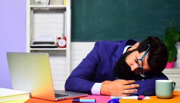 Hard work. School job. Tired male teacher in glasses sleeping at desk in classroom. School break. Overworked exhausted college university student preparing for exam session or test. Sleepy or fatigue