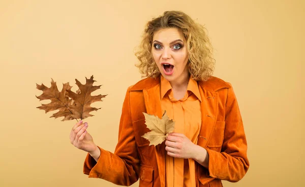 October. Autumn woman in orange shirt and jacket with fall leaves. Autumn fashion for women. Beautiful surprised girl in fashionable wear with autumn leaves. Autumn shopping. Season sales. Discount