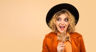 Siyah şapkalı, akçaağaç yapraklı turuncu ceketli sonbahar kadını gözlerini kaçırıyor. Sonbahar yapraklı modaya uygun kadın modeller. Kadınlar için sonbahar modası. Sonbahar indirimi. İndirim. Uzayı kopyala Reklamcılık