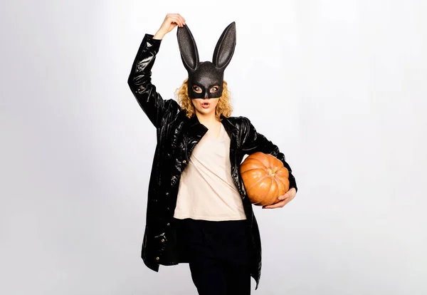 Surprised girl in bunny mask with jack-o-lantern pumpkin. Beautiful female model in black leather jacket at Halloween party. Sexy woman in rabbit mask with Halloween pumpkin. Halloween sale. Discount