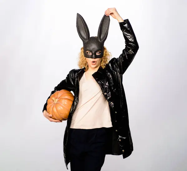 Happy Halloween. Surprised woman in rabbit mask with jack-o-lantern. Sexy girl in black leather jacket with Halloween pumpkin. Blonde girl in bunny mask prepares for Halloween holiday. Trick or treat