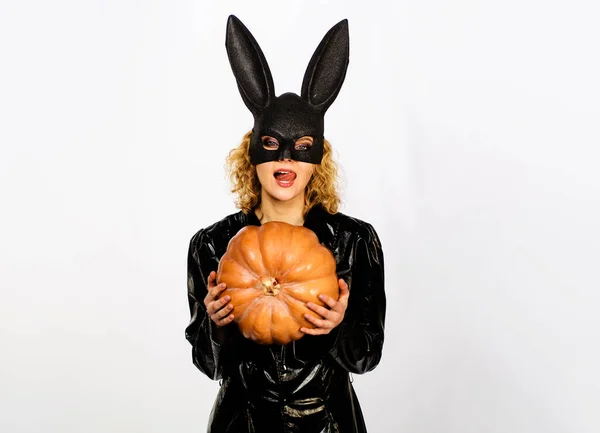 Halloween costume. Sexy girl in bunny mask with pumpkin. Young woman in black leather jacket with Jack-o-lantern. Sensual woman in rabbit ears licking lips with tongue. Bunny woman at Halloween party