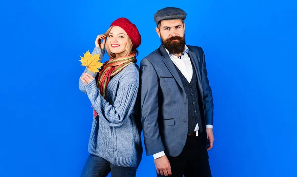 Autumn couple in stylish clothing. Autumn winter fashion. Bearded man in trendy suit standing with young woman in knitted sweater, scarf and hat. Smiling woman with maple leaf. Season sales. Discount