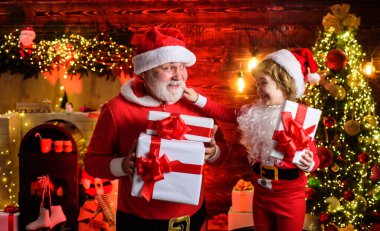 Noel Baba şapkalı küçük çocuk ve evde Noel hediyeli Noel Baba. Noel Baba ve Noel hediyeli çocuk. Noel Baba kostümlü çocuk ve sakallı adam. Noel ve Yeni Yıl Kutlaması